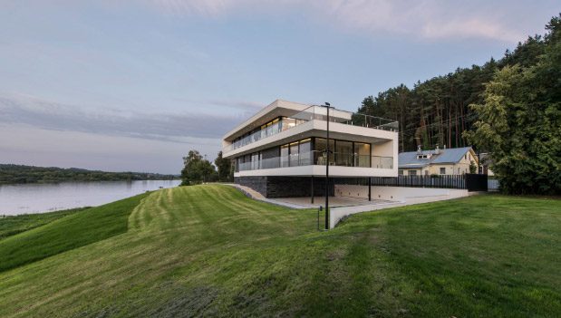 A moradia contemporânea vista do relvado, com a linha de água ao fundo